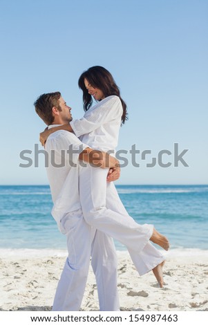Happy man holding woman in arms against ocean on holidays