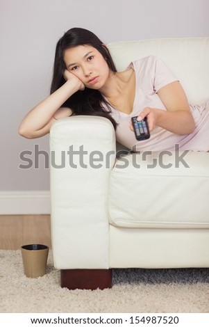 Bored asian girl lying on the sofa watching tv at home in the sitting room