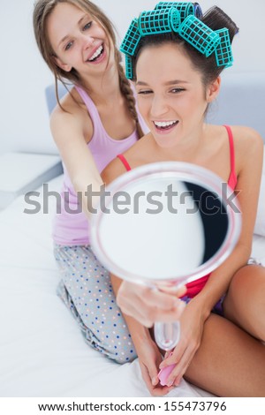 Girl wearing rollers looking in mirror and talking to friend at home on girls night