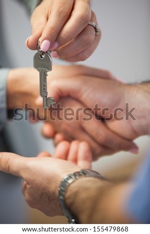 Estate agent giving house key to customer while shaking hands in empty house