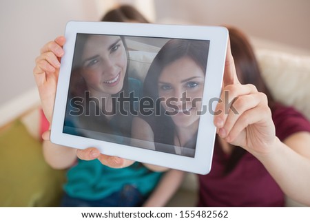 Two happy friends on the couch taking a selfie with tablet pc at home in the living room