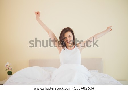 Awakened brunette stretching in her bed in a bedroom on yellow background