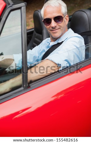 Cheerful handsome man driving his red convertible on a bright day