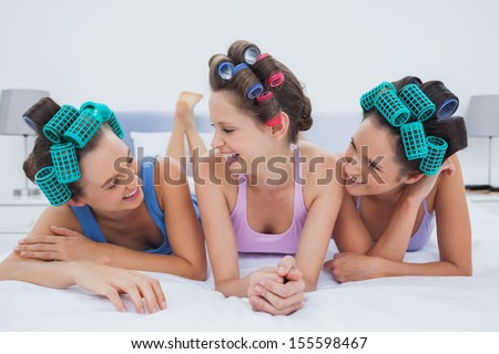 Laughing friends in hair rollers lying in bed and talking at sleepover