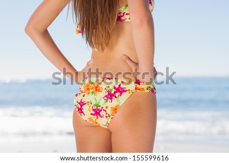 Beautiful woman on the beach in floral bikini standing back to camera