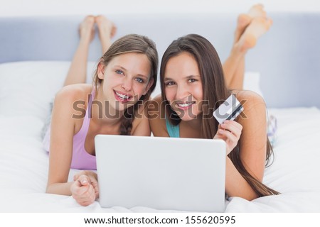 Friends shopping online on bed in their pajamas and looking at camera