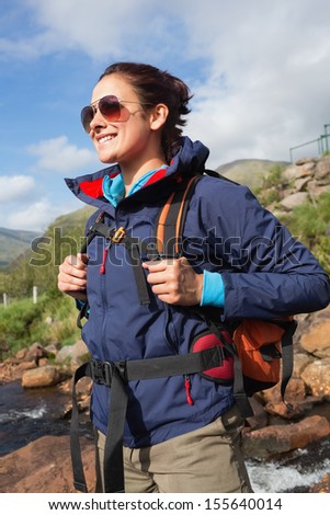 Brunette wearing rain jacket and sunglasses smiling by a river in the countryside