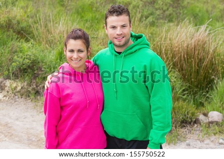 Fit couple looking at camera and embracing on a country trail