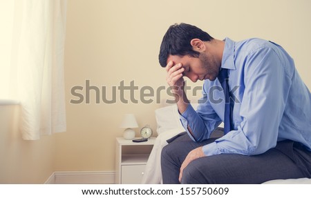 Depressed man sitting head in hands on his bed in a bedroom at home