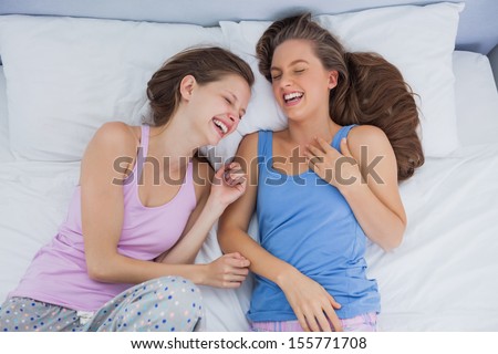Girls wearing pajamas lying in bed and laughing at slumber party