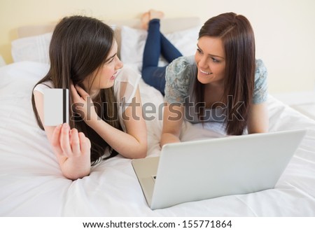 Happy friends using a laptop to shop online lying on bed at home in bedroom