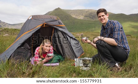 Smiling couple cooking outdoors on camping trip looking at camera