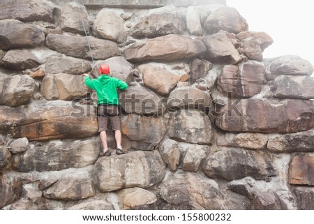 Determined man scaling a large rock face on a bright sunny day