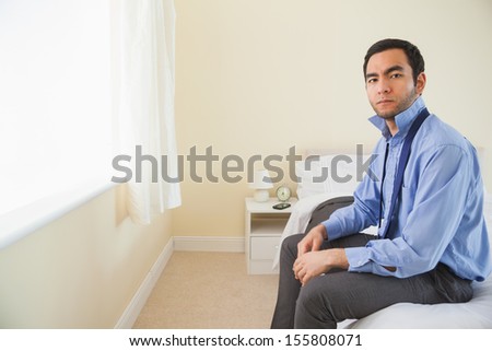 Stern man looking at camera and relaxing sitting on his bed in a bedroom at home