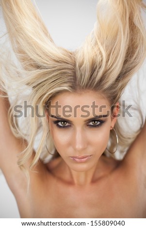 Charming blonde model in black dress posing holding her hair on white background