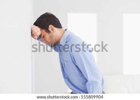 Sad man with fist clenched leaning his head against a wall