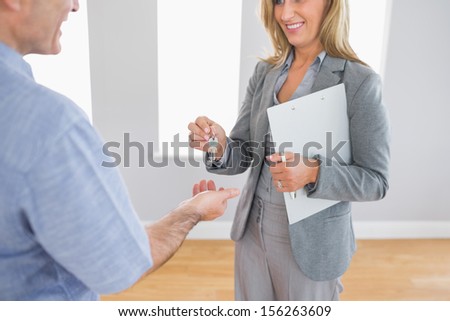 Close up of a smiling blonde realtor delivering a key to a buyer mature customer standing in an empty room