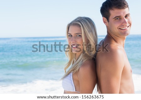 Young smiling couple standing back to back at the beach