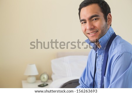 Content man looking at camera and relaxing sitting on his bed in a bedroom at home