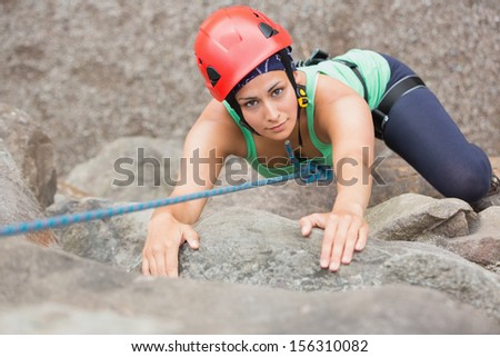 Determined girl climbing rock face looking at camera