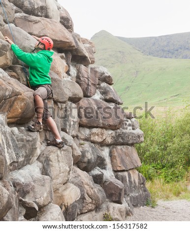Focused man ascending a large rock face with mountains and countryside in background