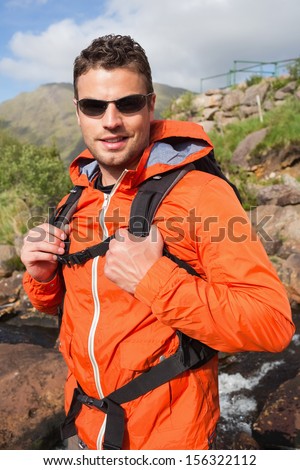 Man wearing rain jacket and sunglasses smiling at camera in the countryside