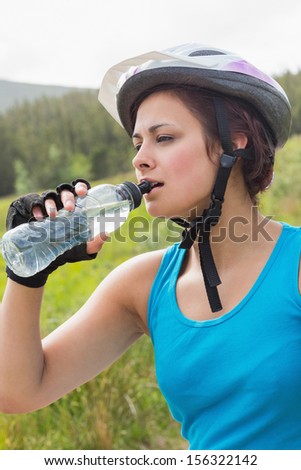 Fit woman wearing bike helmet drinking water in the countryside
