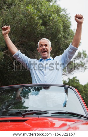 Smiling mature man enjoying his red convertible on a bright day