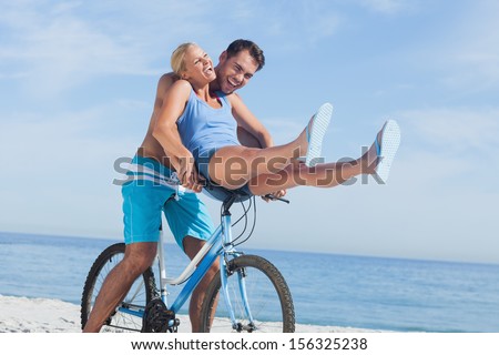 Happy Man Giving Girlfriend A Lift On His Crossbar Of Bike On The Beach