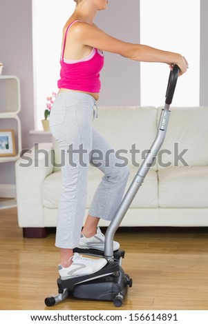 Side view of sporty woman training on step machine in bright living room