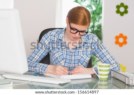 Redhead writing on notepad at her desk working from home