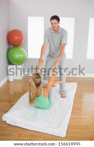 Smiling physiotherapist helping patient doing exercise in bright office
