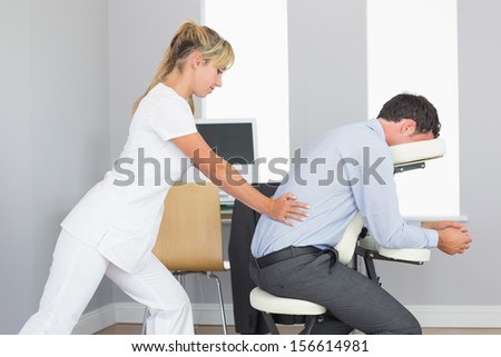 Masseuse treating clients lower back in massage chair in bright room