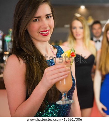Attractive woman standing in front of her friends holding cocktail looking at camera