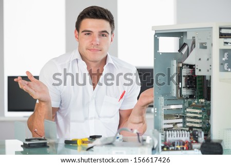 Confused computer engineer sitting behind open computer in bright office