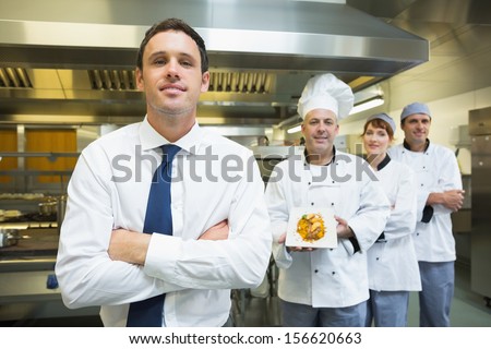 Young Restaurant Manager Posing In Front Of Team Of Chefs Smiling At Camera