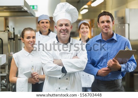 Head Chef Posing With The Team Behind Him In A Professional Kitchen