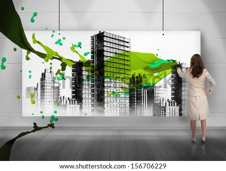 Rear view of businesswoman painting city on screen with green splashes