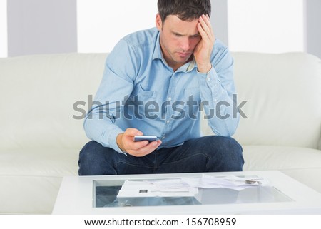 Upset casual man using calculator paying bills in bright living room