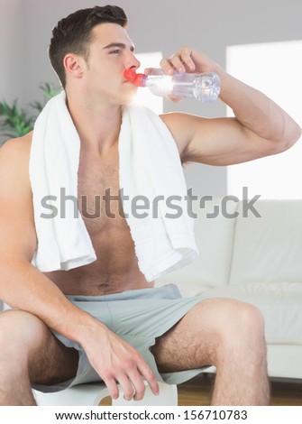 Handsome sporty man drinking from water bottle in bright living room