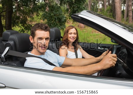 Happy couple driving in a silver convertible smiling at camera