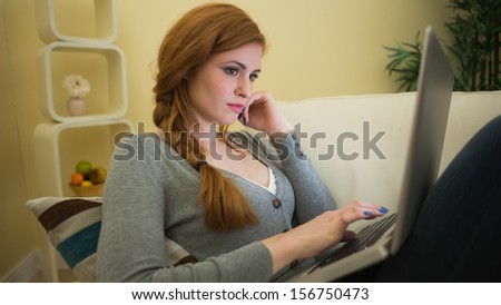 Pretty redhead sitting on the sofa using her laptop at night at home in the sitting room