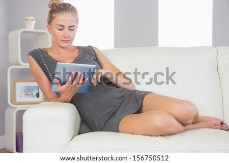 Casual calm blonde relaxing on couch using tablet in bright living room