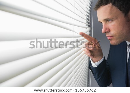 Stern attractive businessman spying through roller blind in dark room