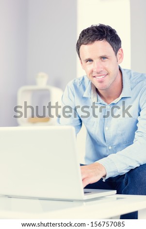 Smiling casual man looking at camera using laptop in bright living room