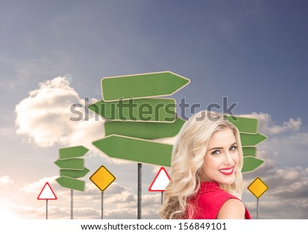 Composite image of attractive woman standing back to camera looking over shoulder in front of road signs in sky