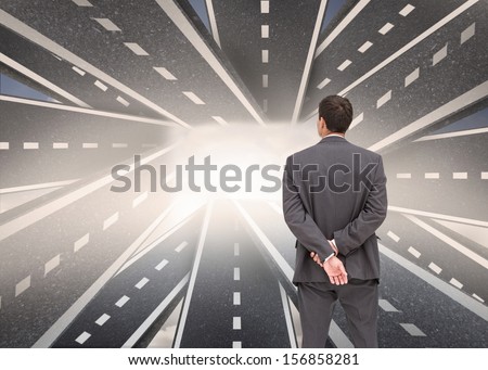 Composite image of businessman standing with hands behind back with streets running together in background
