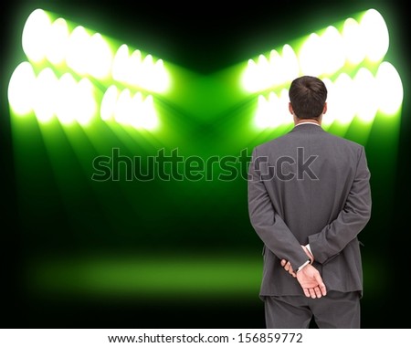 Composite image of businessman standing with hands behind back looking at green spot lights on black background