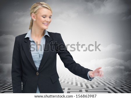 Composite image of smiling businesswoman showing something in front of huge maze in background