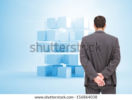 Composite image of businessman standing with hands behind back looking at plastic blue cubes in the background